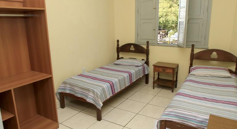 Quarto de unidade de acolhimento institucional para população em situação de rua, com duas camas, uma cabeceira e um armário.