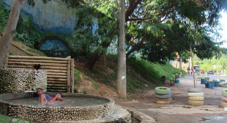 Três crianças brincam em uma piscina natural construída em volta de uma nascente