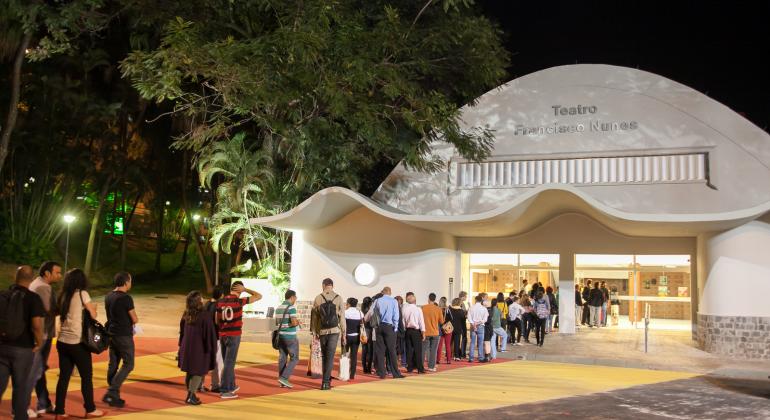 Teatros Municipais recebem 44ª Campanha de Popularização Teatro Francisco Nunes, no Parque Municipal, à noite, com fila de cerca de 50 pessoas