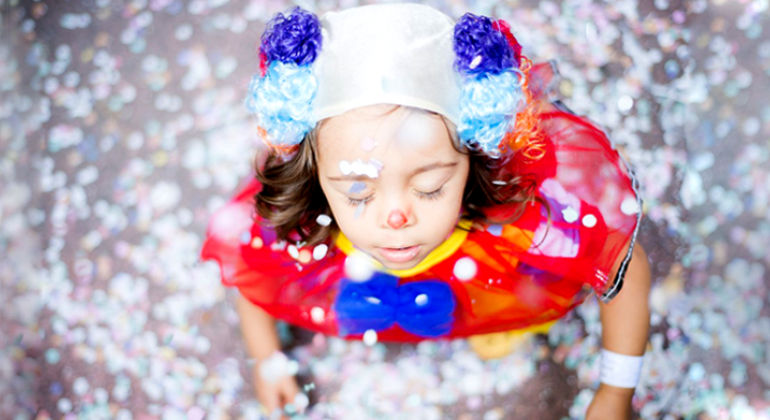A programação do BH é da Gente – Savassi entra no ritmo do carnaval neste domingo, 21/01, com o ensaio do bloco Charanga das Padês. Foto: Bruna Tassis Criança fantasiada de palhaço fecha os olhos; ela está em meio a confetes de papel.