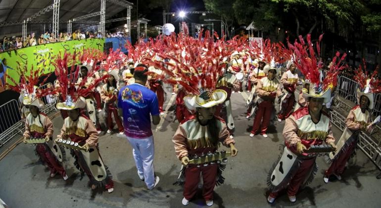 Mais de trinta membros da Escola de Samba Acadêmicos de Venda Nova, campeã do Carnaval de Belo Horizonte de 2017, tocando instrumentos musicais; a fila da frente tem quatro membros com chocalhos. 