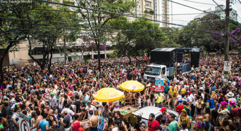 Foliões lotam rua com trio elétrico em bloco de rua.