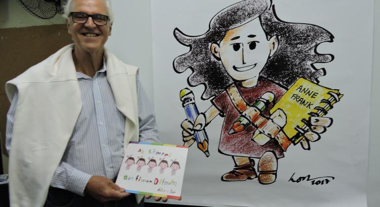Cartunista LOR posa ao lado de uma caricatura de Anne Frank, menina dos livros que dá nome à escola