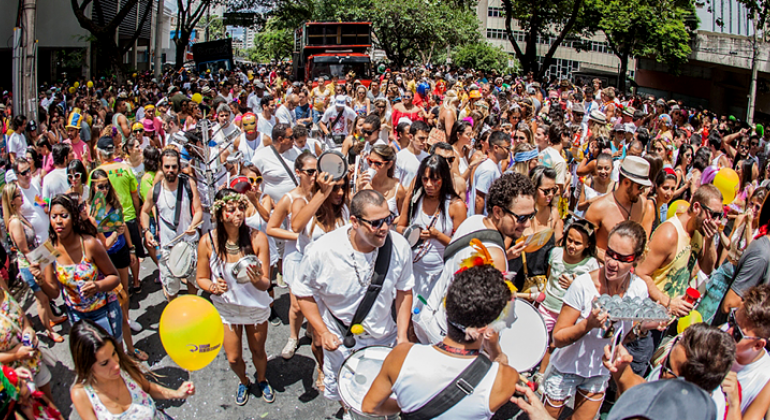 Conselheiros tutelares irão orientar sobre como lidar com crianças no Carnaval 2018 na entrega de credenciais para o trabalho ambulante. Foto: Divulgação/PBH Membros de um bloco de carnaval toca instrumentosmusicais; um pouco atrás, mais de trezentas pessoas acompanham; mais ao fundo há a presença de um caminhão de som.