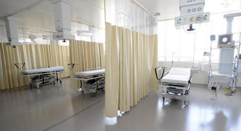 Três macas e três cortinhas acompanhadas de aparelhos médicos em ambiente hospitalar