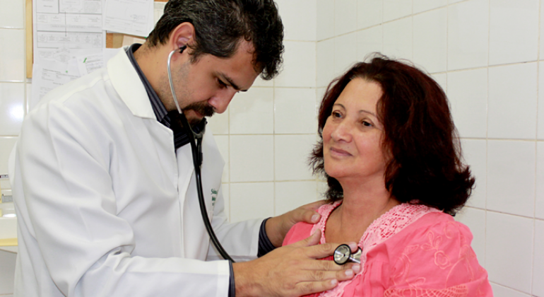 Médico examina coração de paciente com estetoscópio.