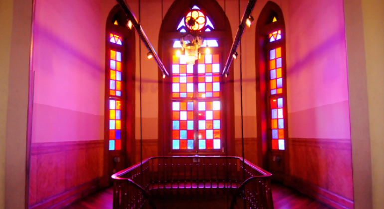 Interior do Museu da Moda, com vitrais nas cores azul e vermelho em sala com escada.