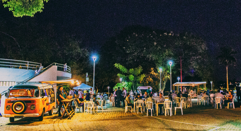 Vigilância Sanitária promove na quarta-feira, dia 24/1, curso de capacitação de normas para comércio de alimentos em vias públicas. Foto: Ricardo Laf/PBH Praça da Pampulha mostra food truck e pessoas sentadas em mesas, conversando.