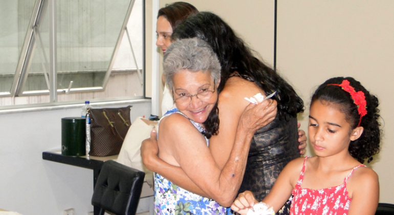 Projeto “Para Elas – Por Elas, Por Eles, Por Nós” transforma a realidade de mulheres vítimas de violência ou que em vulnerabilidade social. Foto: Naara Dias Duas mulheres se abraçam, uma menina está mais à frente e à direita e uma mulher, atrás e à esquerda.