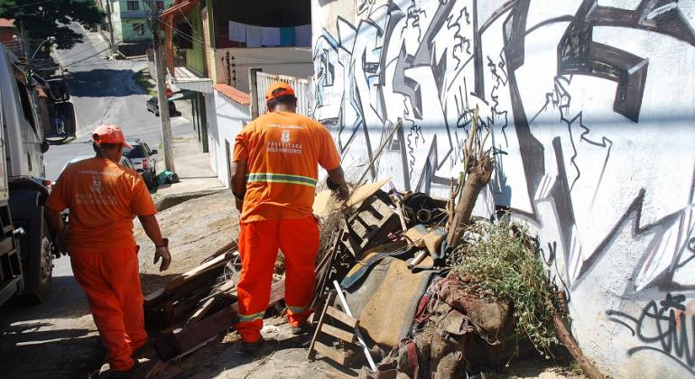 Ações preventivas de combate ao mosquito Aedes aegypti são realizadas na Região Nordeste. Foto: Mara Damasceno/PBH Dois garis retiram lixo acumulado ao lado de muro da Região Nordeste.