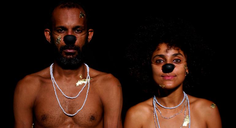 Dois atores negros, homem e mulher, sem camiseta e com nariz de palhaço.