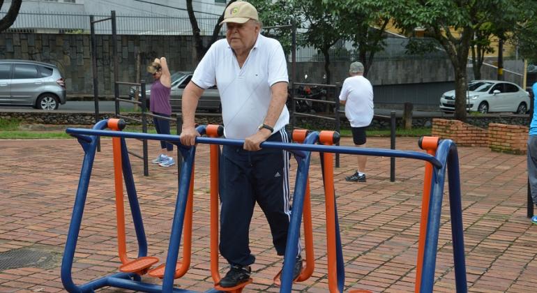 Senhor de idade de boné e camisa polo branca faz exercícios em Academia a Céu Aberto.