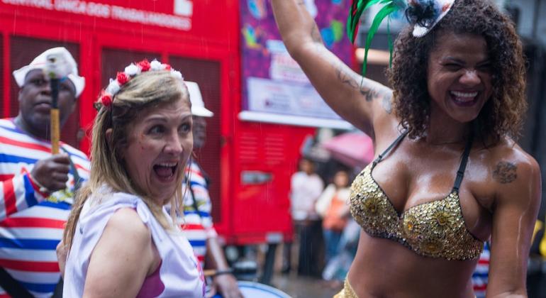Duas mulheres sorriem com adereços de carnaval. 