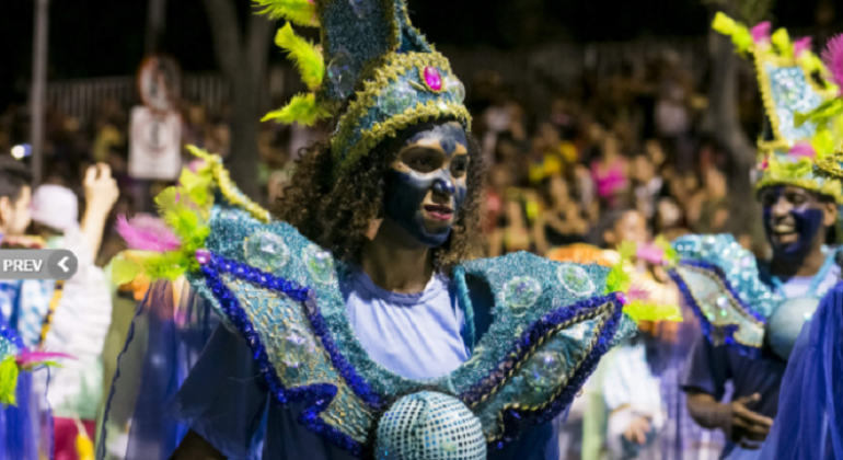Membro de Bloco Caricato academia de Samba por Acaso com fantasia azul e adereços nas cores verde e amarelo.