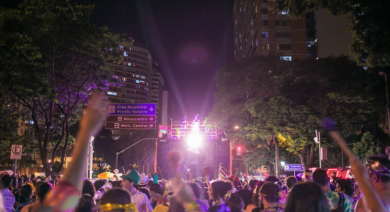 Confira os principais eventos gratuitos que acontecem em BH neste fim de semana, de 2 a 4 de fevereiro. Foto: André Paiva, Cacá Lanari e Marco Túlio Pires Bloco Chama o Síndico com caminhão elétrico e prédio ao fundo, muitas pessoas à frente e placas indicativas de trânsito à direita.