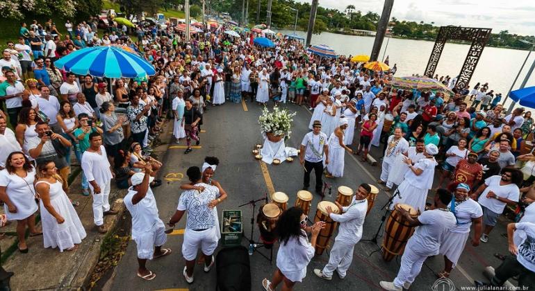 Mais de vinte pessoas vestidas de branco, do Candomblé, homenageiam Iemanjá na beira da Lagoa da Pampulha. Mais de cem pessoas assistem.