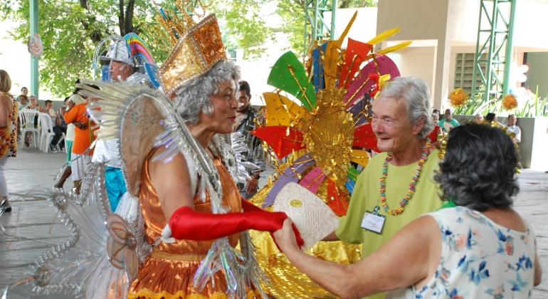 Duas idosas com fantasias de carnaval brincam com duas idosas com roupas comuns.