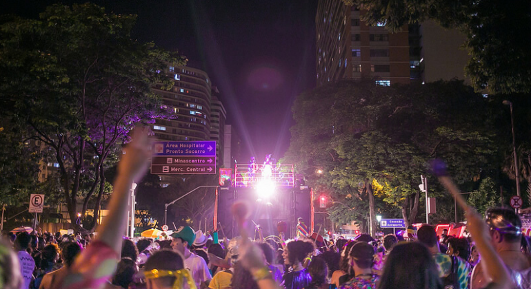 Foliões com as mãos para cima desfilam na Avenida Afonso Pena à noite.