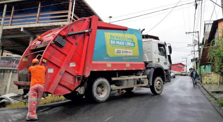 Caminhão de recolhimento de lixo sobe a rua, junto a ele, funcionário da SLU.