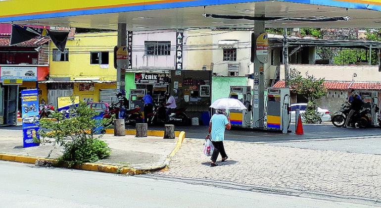 Posto de Combustível com fregueses e frentistas, durante o dia.