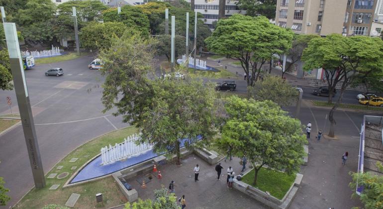 Praça da Savassi durante o dia, com movimento de carros e gente. 