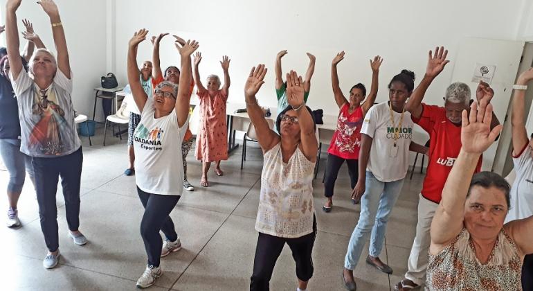 Amigas ganham qualidade de vida ao frequentar as atividades esportivas e recreativas do programa Vida Ativa, desenvolvido pela PBH. Foto: Divulgação PBH Cerca de 10 senhoras fazem ginástica com mãos levantadas; atividade faz parte do programa Vida Ativa.