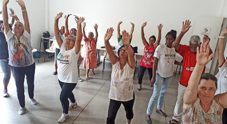 Cerca de 10 senhoras fazem ginástica com mãos levantadas; atividade faz parte do programa Vida Ativa.