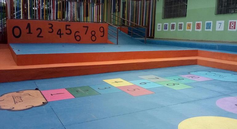 Pátio de escola municipal que atende a Educação Infantil, com chão pintado com o jogo da amarelinha em cores diversas.