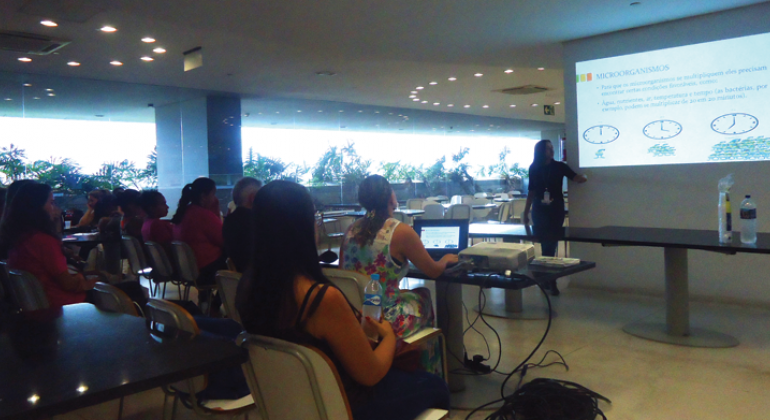 Curso sobre práticas de manipulação de alimentos é oferecido pela Vigilância Sanitária na Cidade Administrativa. Foto: Divulgação PBH Mais de 10 pessoas sentadas assistem à aula sobre manipulação de alimentos.