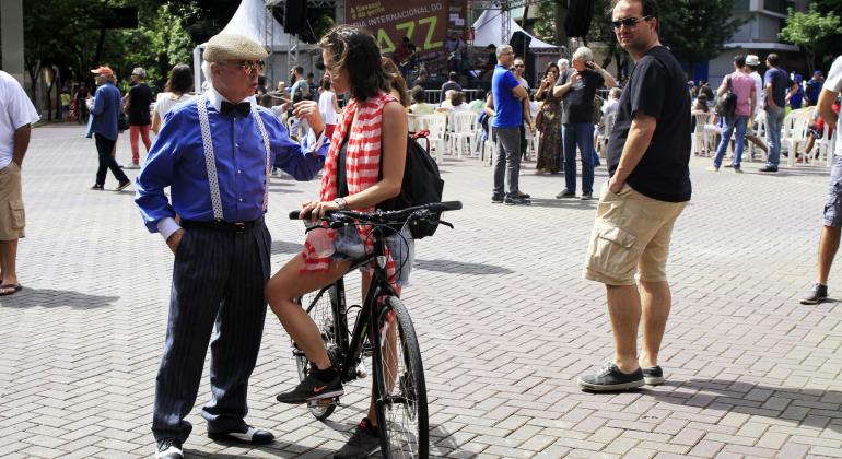 Senhor de suspensórios e boina conversa com jovem de bicicleta no cruzamento das avenidas Cristóvão Colombo e Getúlio Vargas. Pessoas transitam ao redor.