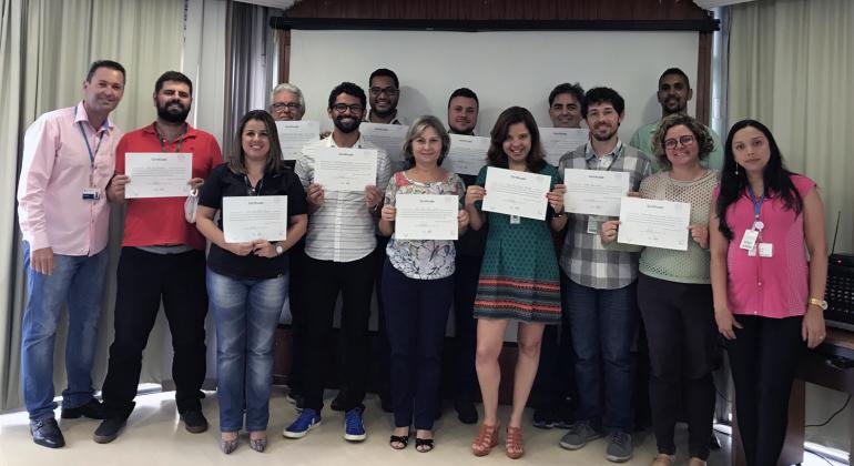 Treze servidores, com certificados em mãos, posam para foto ao lado de um dos professores.