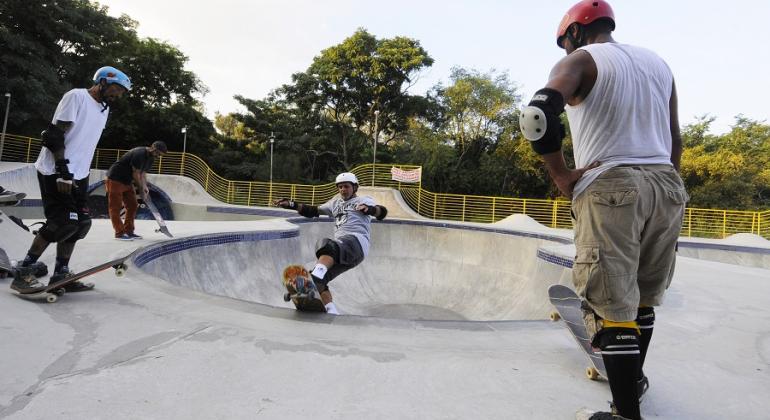 Três skatistas praticam skate na pista do Parque Municipal Lagoa do Nado.