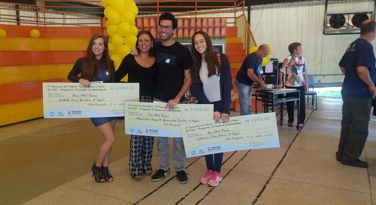 BHTrans promove concurso de vídeos "O Trânsito e o Valor da Vida" com objetivo de promover uma cidade com trânsito mais humano. Foto: Divulgação PBH Quatro vencedores de concurso de vídeo "O Trânsito e o Valor da Vida", promovido pela BHTrans, exibem três cheques grandes.