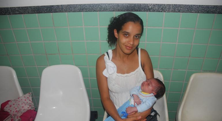 Unidade coletora de leite humano do Centro de Saúde Vila Maria contabiliza doação de 58 litros de leite humano. Foto: Melissa Reis Mlher segura recém-nascido no colo em cadeira de centro de saúde.