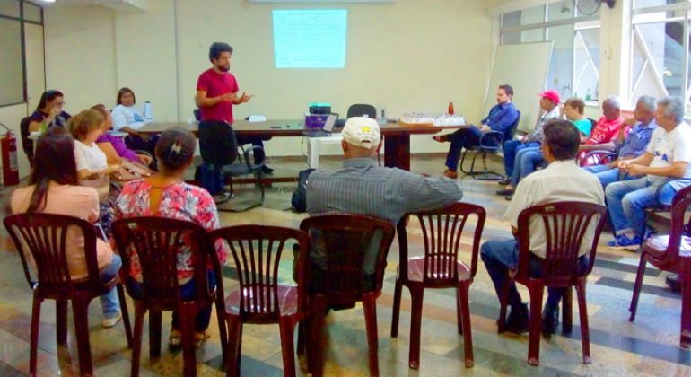 Homem apresenta projeto, de pé, para mais de vinte pessoas sentadas, em uma sala.