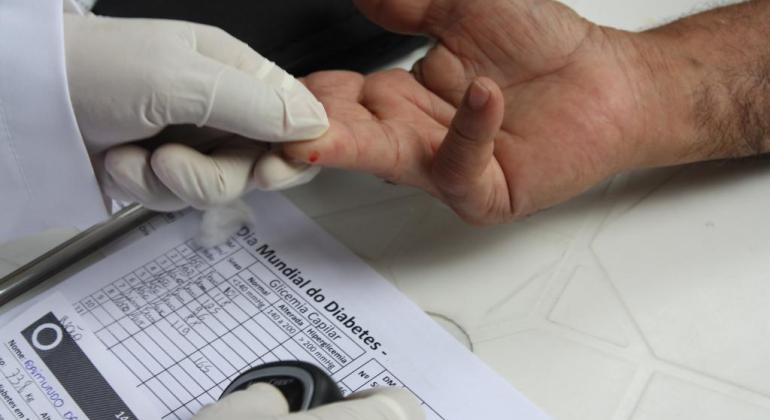 Prefeitura compra 3.500 aparelhos para medição de glicose Duas mãos na foto. Uma, de um servidor da saúde, usando luva, mede a glicose de paciente
