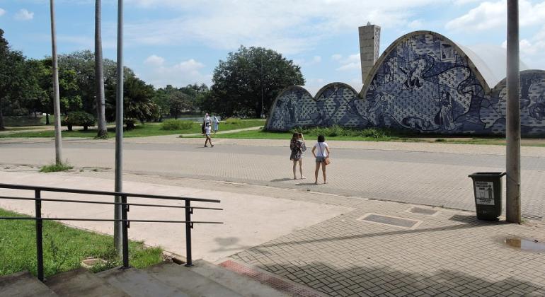 Duas pessoas atravessam a rua em direção à Igrejinha da Pampulha. À frente, escada da Praça Dino Barbieri.