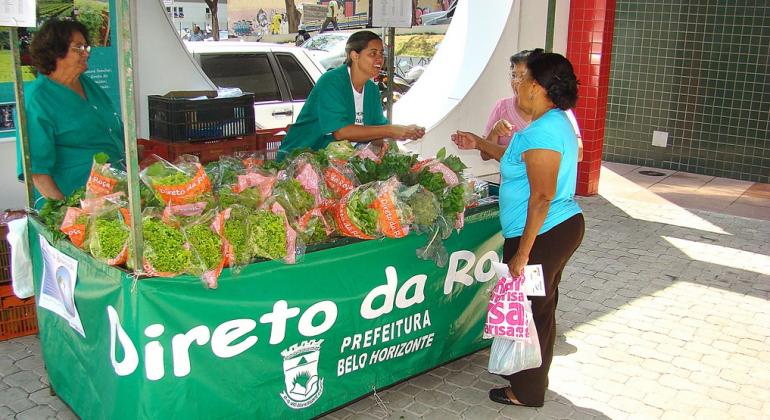 Resultado do edital de concorrência para seleção de agricultores familiares foi publicado pela Prefeitura no DOM de 6 de março. Foto: Divulgação PBH Duas mulhers compram alfaça em barraquinha do Programa Direto da Roça.