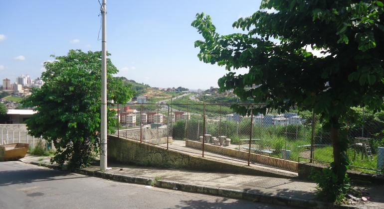 Quadra esportiva na Vila São José passará por melhorias Quadra São José em dia de sol antes do início das obras. Há uma grade e mato no local.