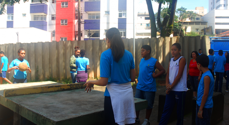 Cerca de oito alunos jogam pingue-pongue em pátio de escola municipal.