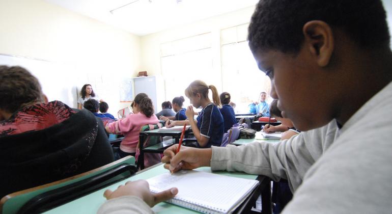 Alunos em uma sala de aula com professora ao fundo