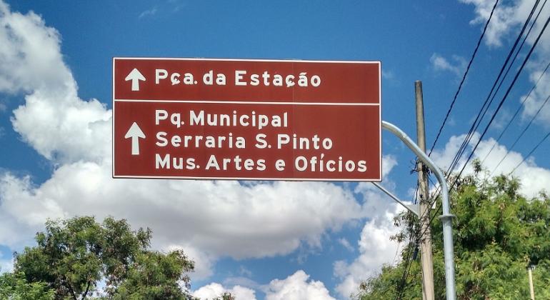 Placa de sinalização turística com os dizeres: Praça da Estação, Parque Municipal, Serraria S. Pinto e Mus. de Artes e Ofícios.