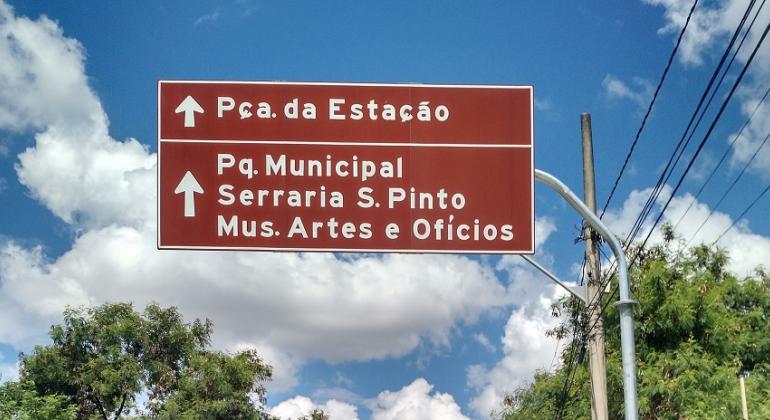 Foto: Divulgação PBH Placa de sinalização turística com os dizeres: Praça da Estação, Parque Municipal, Serraria S. Pinto e Mus. de Artes e Ofícios.