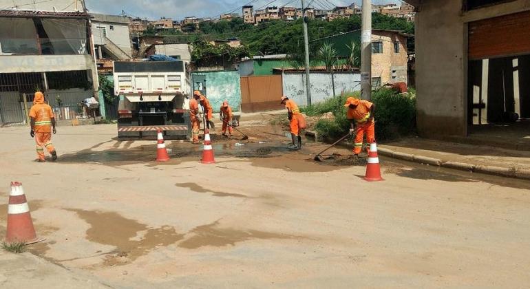 Garis da SLU recolhem lama de uma esquina próximo a um caminhão.