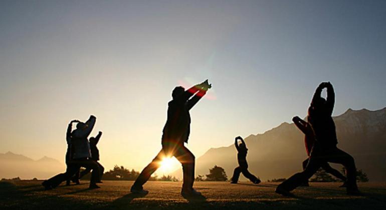 Cinco pessoas fazem alongamento em parque com pôr do sol ao fundo. 