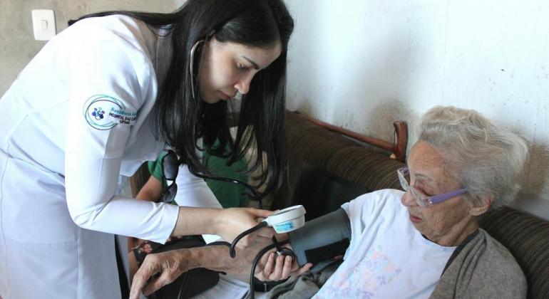 Médica afere pressão de paciente idosa em atendimento domiciliar. 