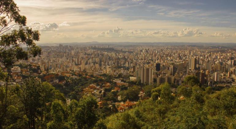 Mais de quinhentos prédios de Belo Horizonte, com área verde à frente e céu azul no fundo, durante o dia. 