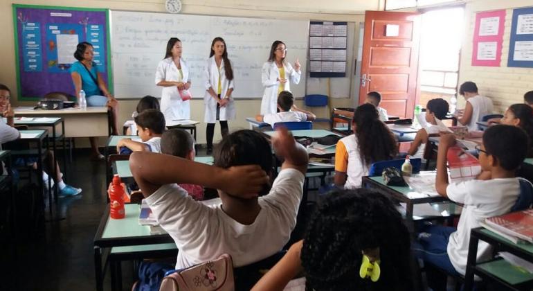 Centro de saúde e escola municipal da Região Noroeste se uniram para informar crianças e adolescentes sobre o combate à Febre Amarela. Foto: Divulgação PBH Três técnicas de saúde dão palestra sobre o combate à Febre Amarela em sala de aula com professora e mais de dez alunos.