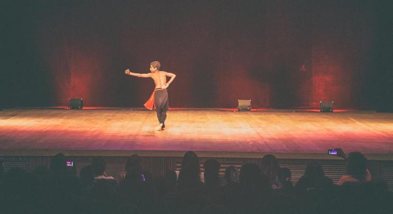 Garoto se apresenta no palco do Teatro Francisco Nunes usando uma calça preta e tecido vermelho amarrado na cintura.