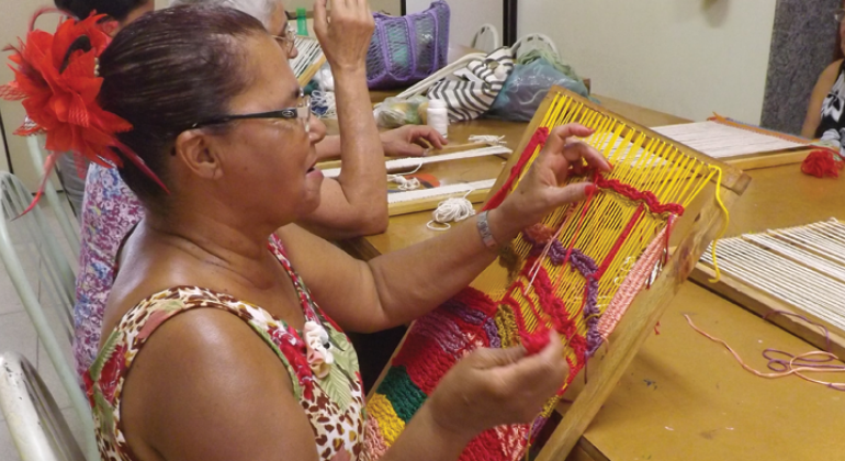 Oficina A Arte de Tecer propõe uma imersão no universo da tecelagem e do trançado brasileiro no Centro Cultural Venda Nova. Foto: Sabrina Damas e Gustavo Pires/PBH Mulher faz tecelagem com linhas coloridas em tear.